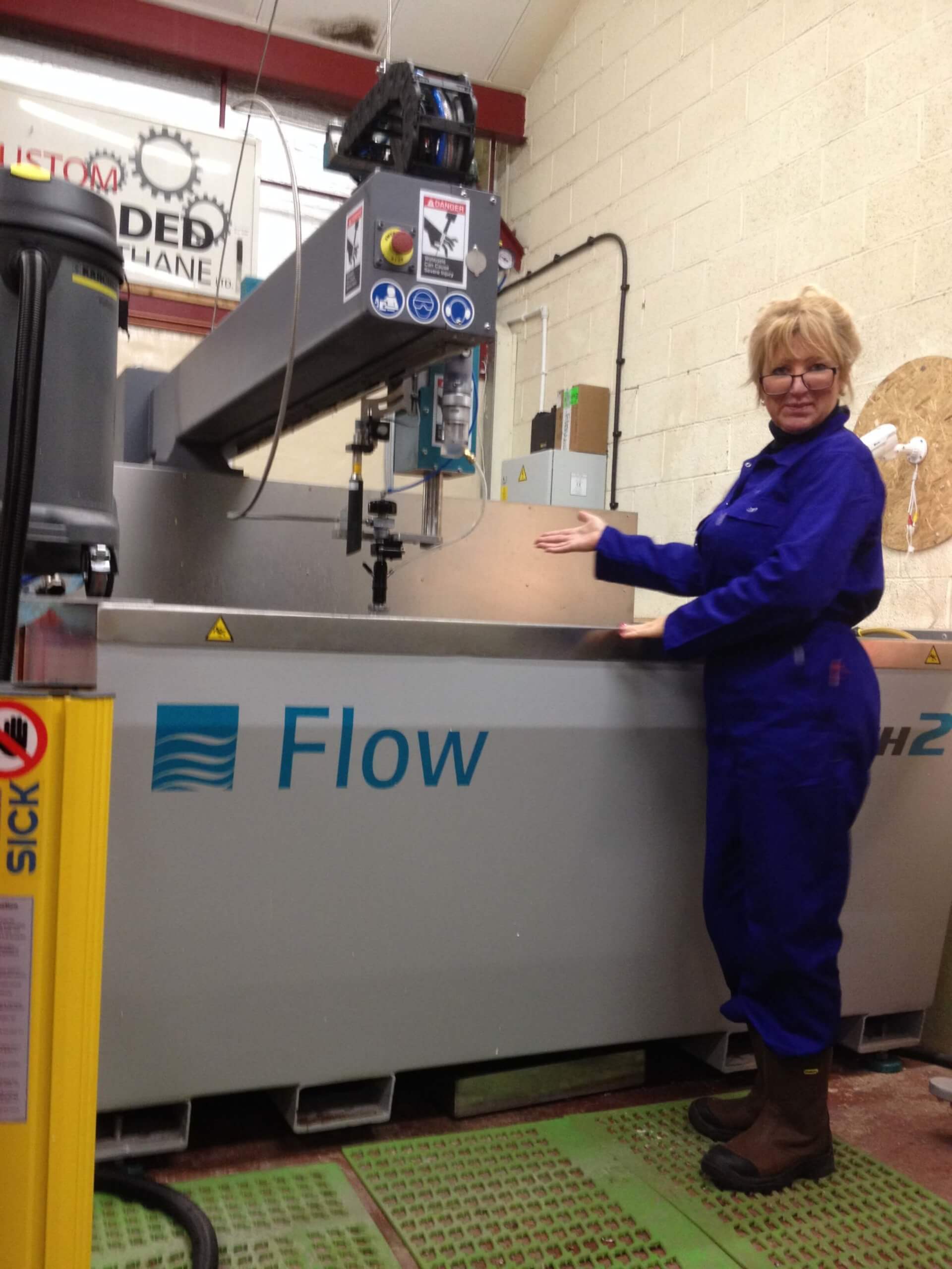 Machine labeled "Flow" in workshop, operated by person in coveralls.
