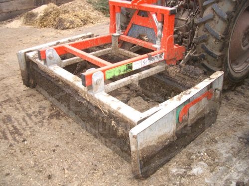 Metal grader attached to tractor, smoothing dirt on farm.