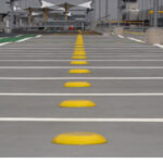 Yellow dome markers line outdoor walkway near structures.