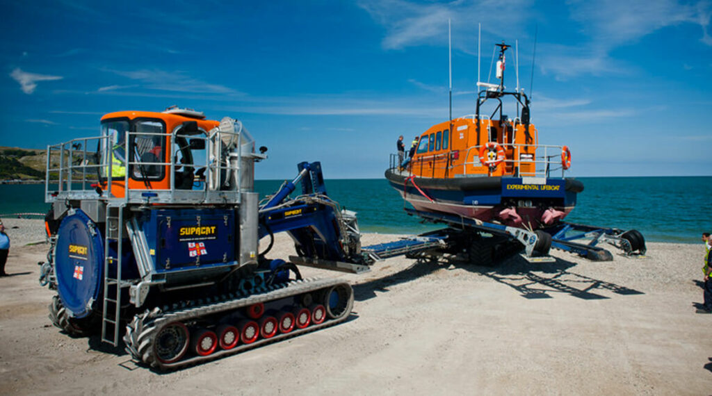 Tracked vehicle launching lifeboat, beachside, bright sunny day.