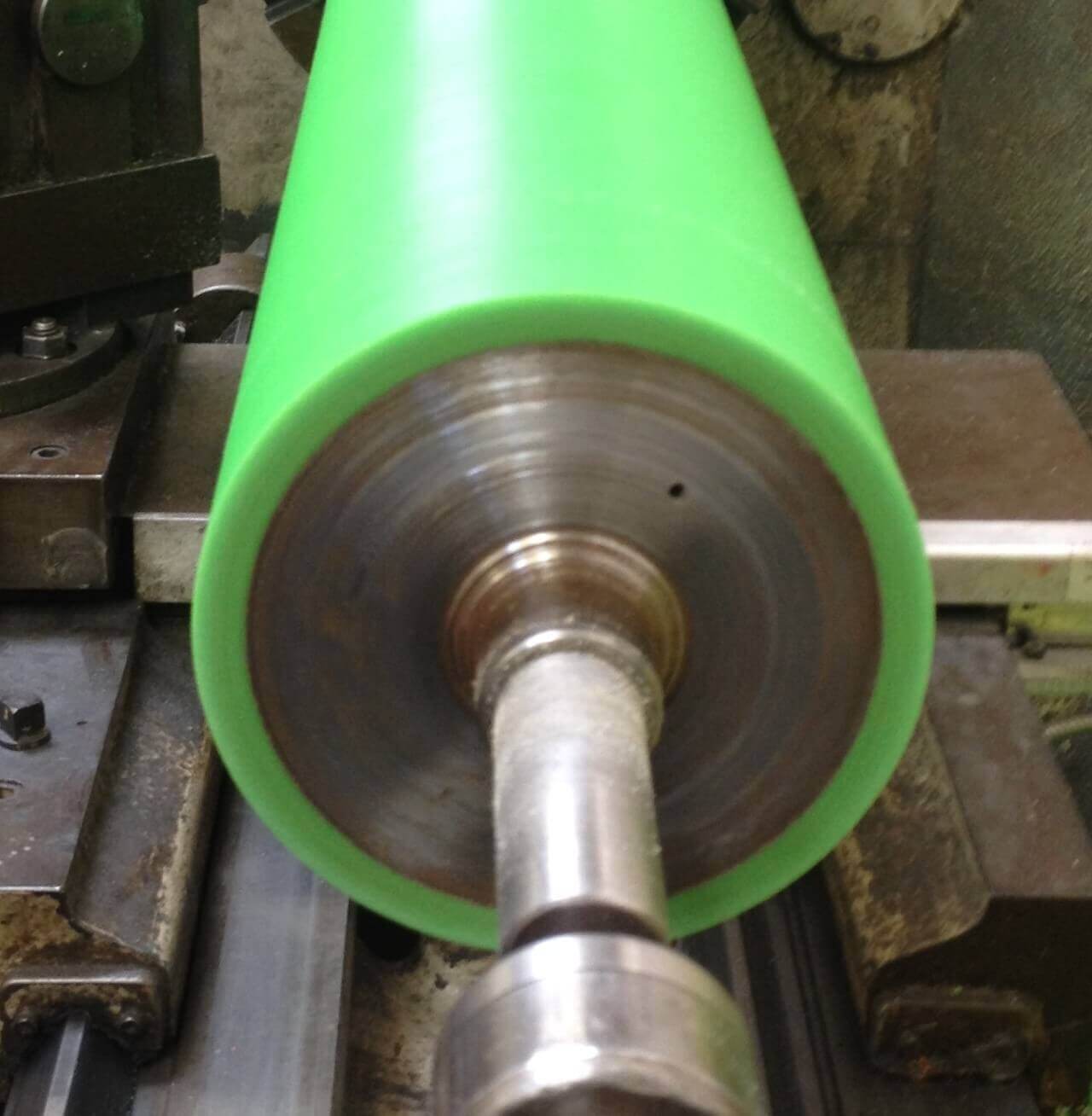 Green cylinder rotating on industrial lathe machine table.