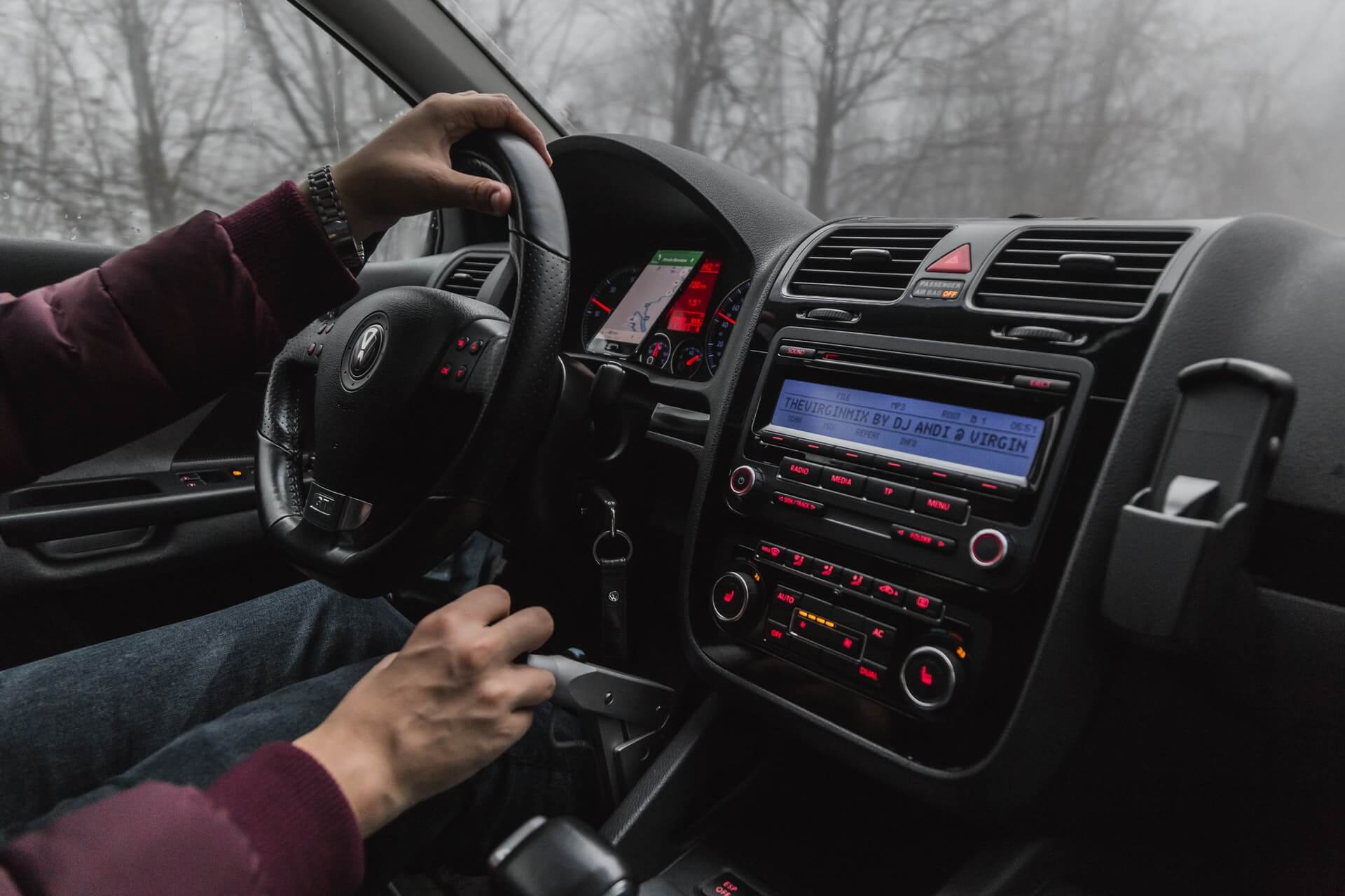 Driver holding steering wheel in foggy car interior.
