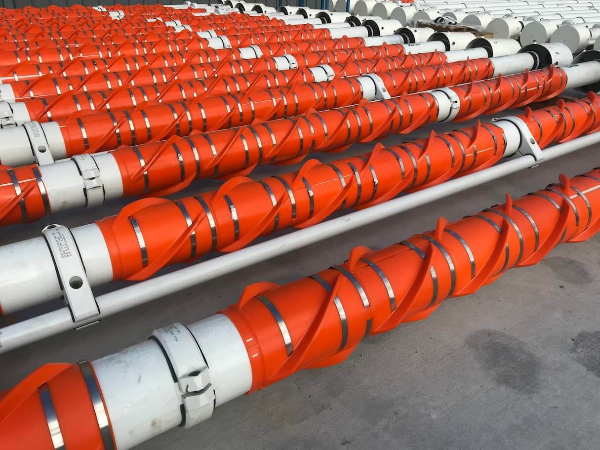 Orange buoyancy modules attached to pipes, lined on concrete ground.