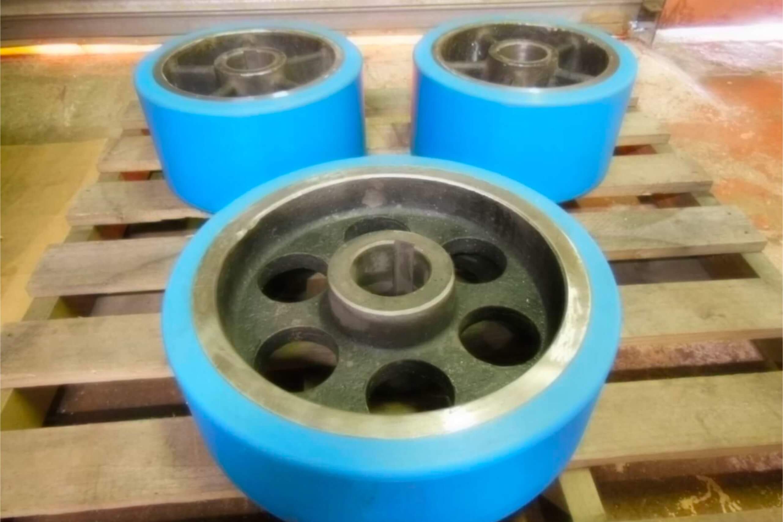 Blue industrial wheels resting on wooden pallet indoors.