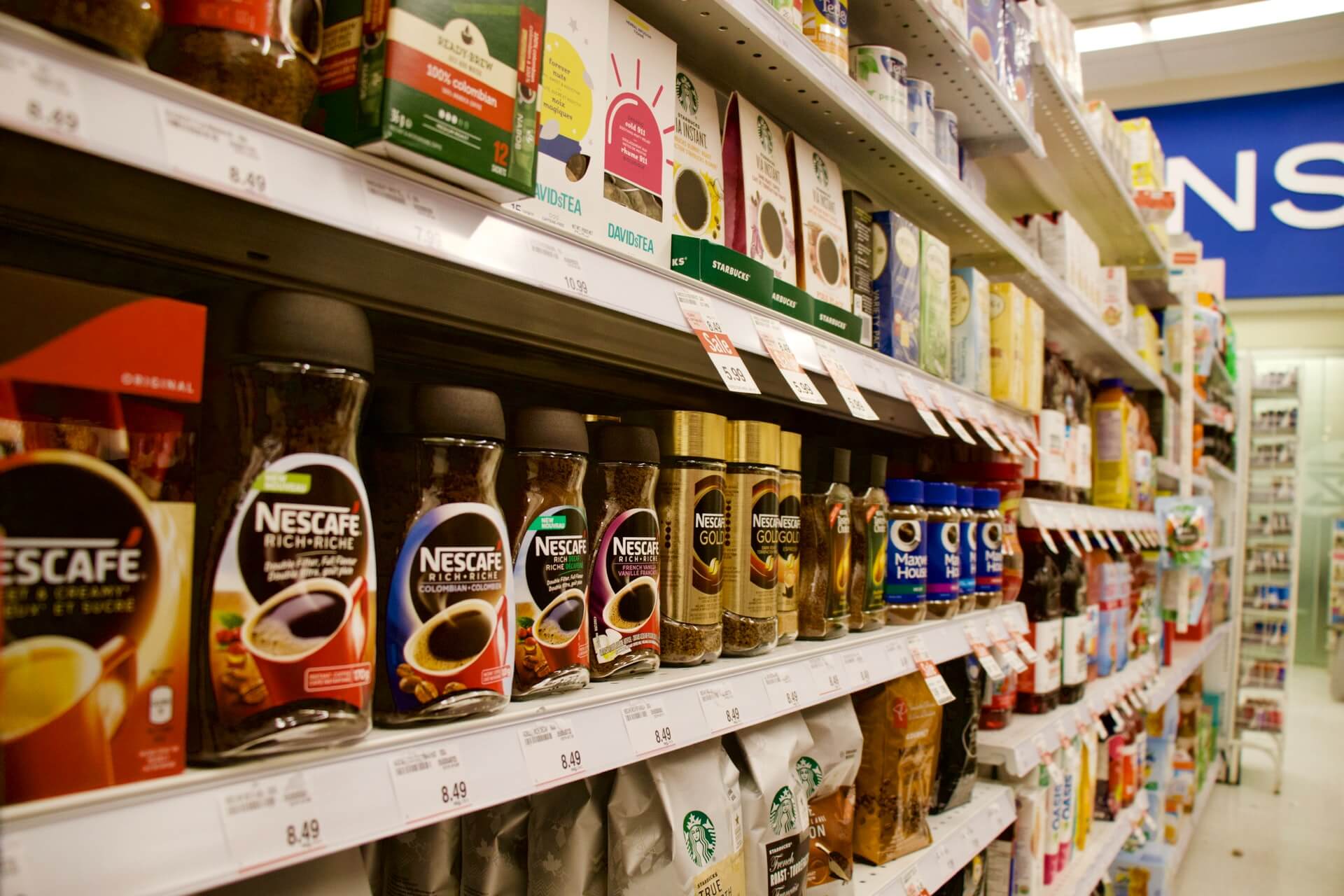 Coffee jars lined on supermarket shelf, surrounded by various products.