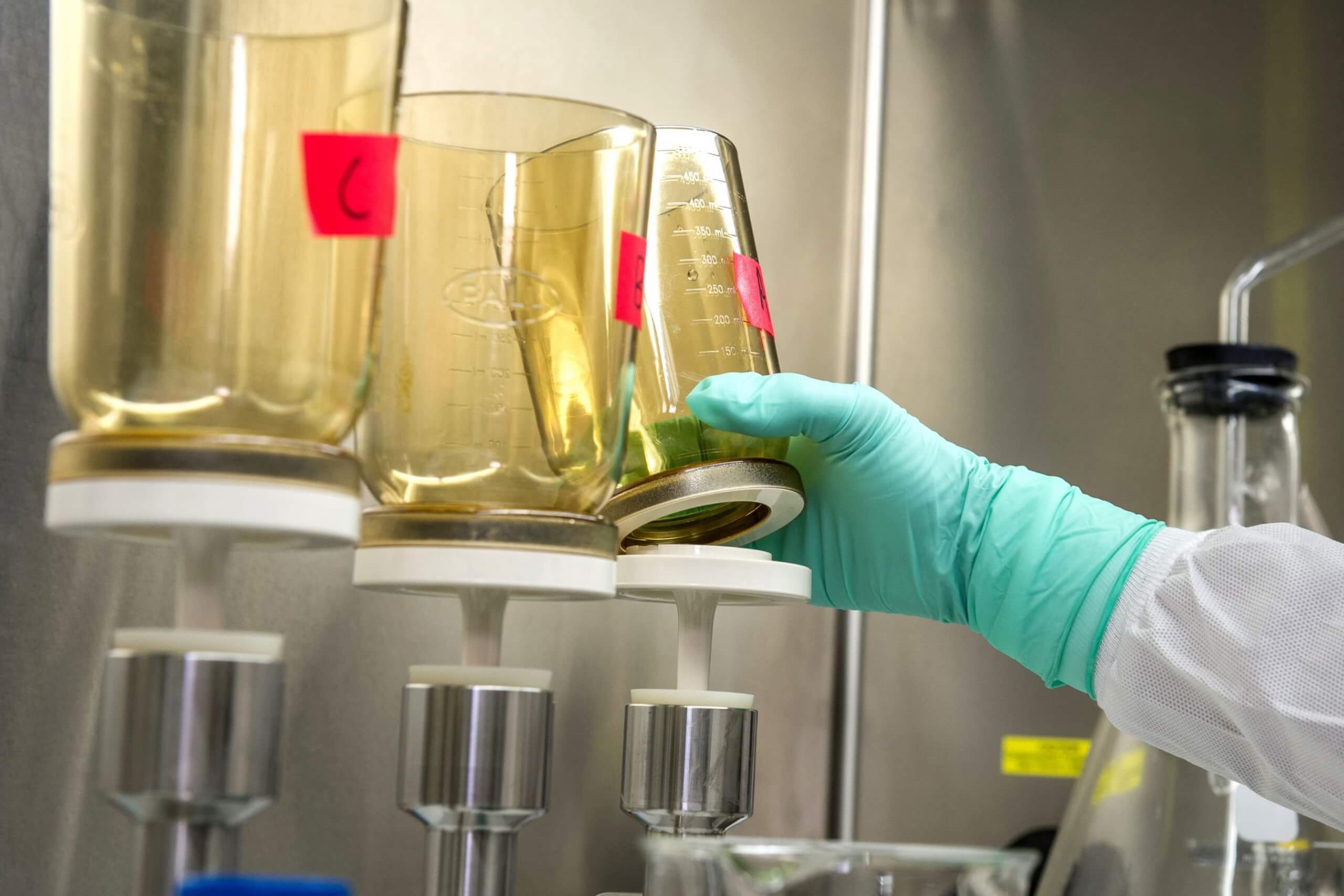 Gloved hand adjusts funnel in stainless steel lab setup.