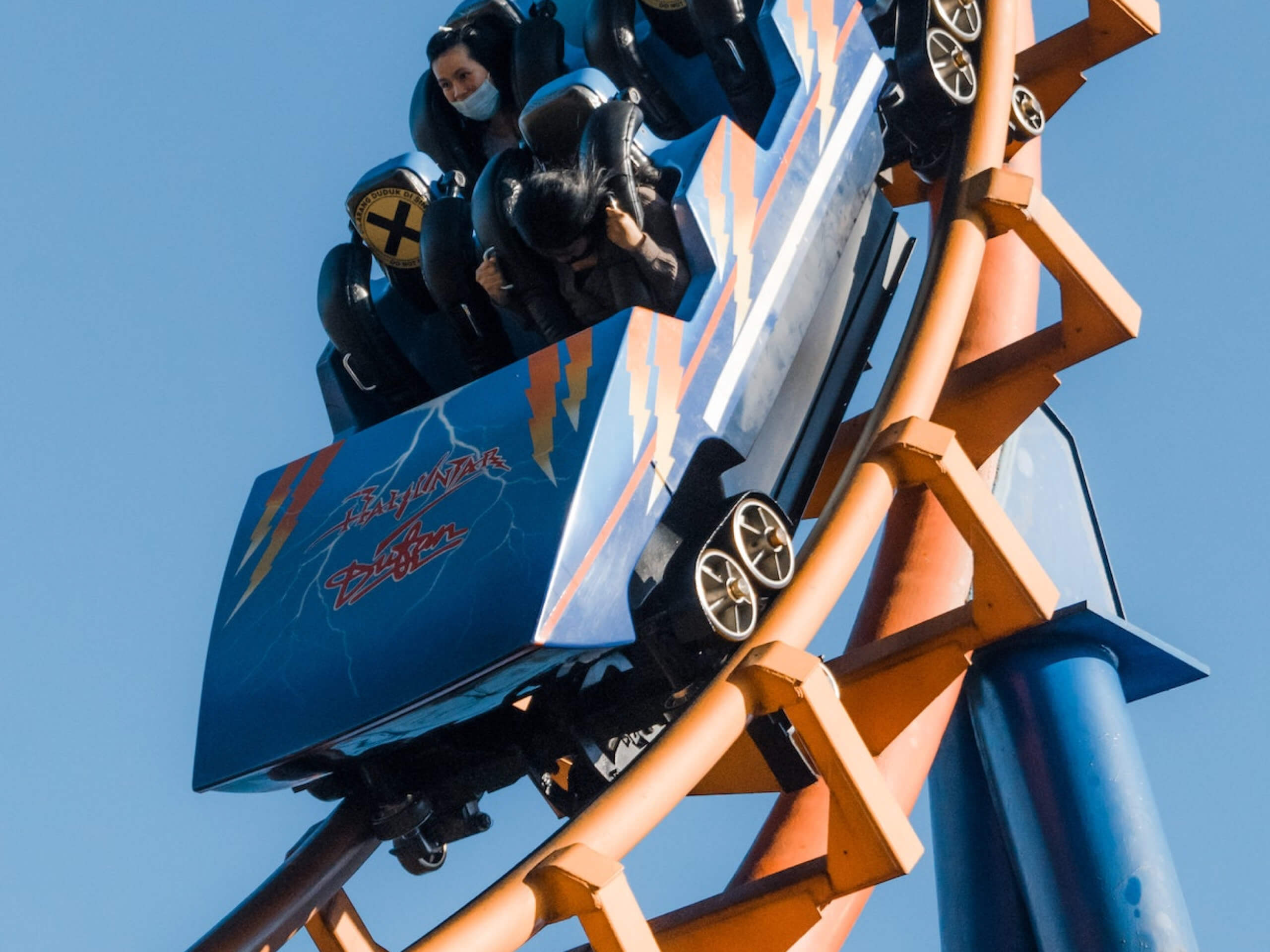 Roller coaster descends steep track, riders scream, clear sky backdrop.