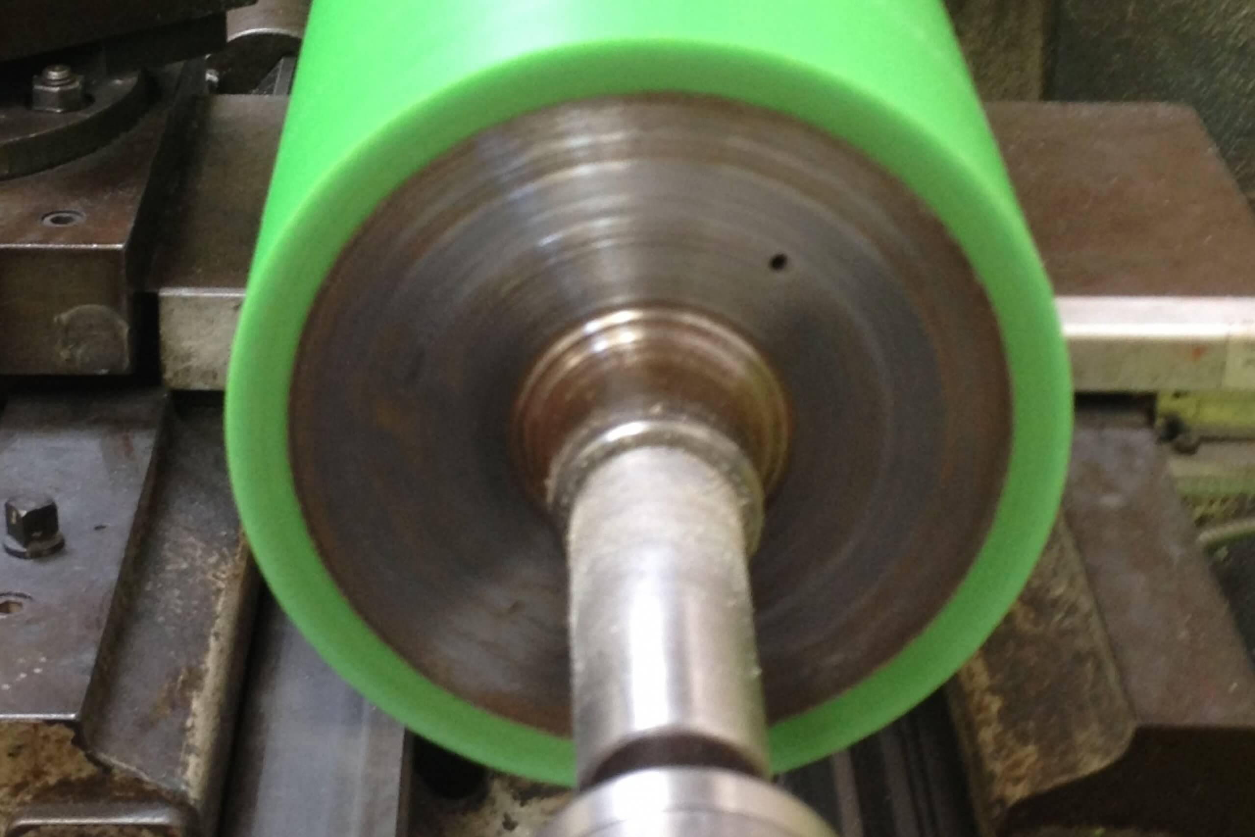 Green cylinder rotates on a metal lathe in a workshop.