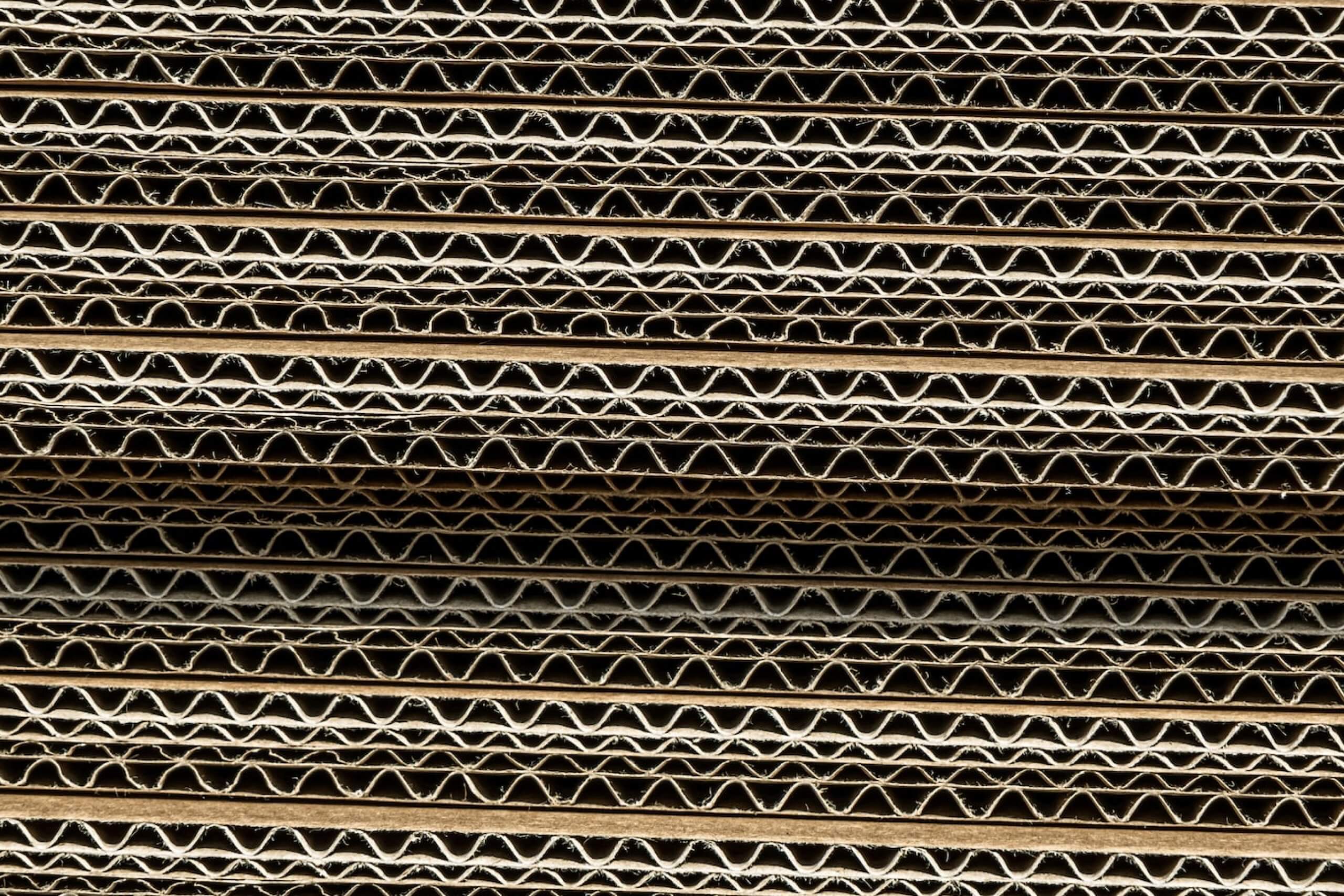 Corrugated cardboard layers stacked, showing wavy interiors.