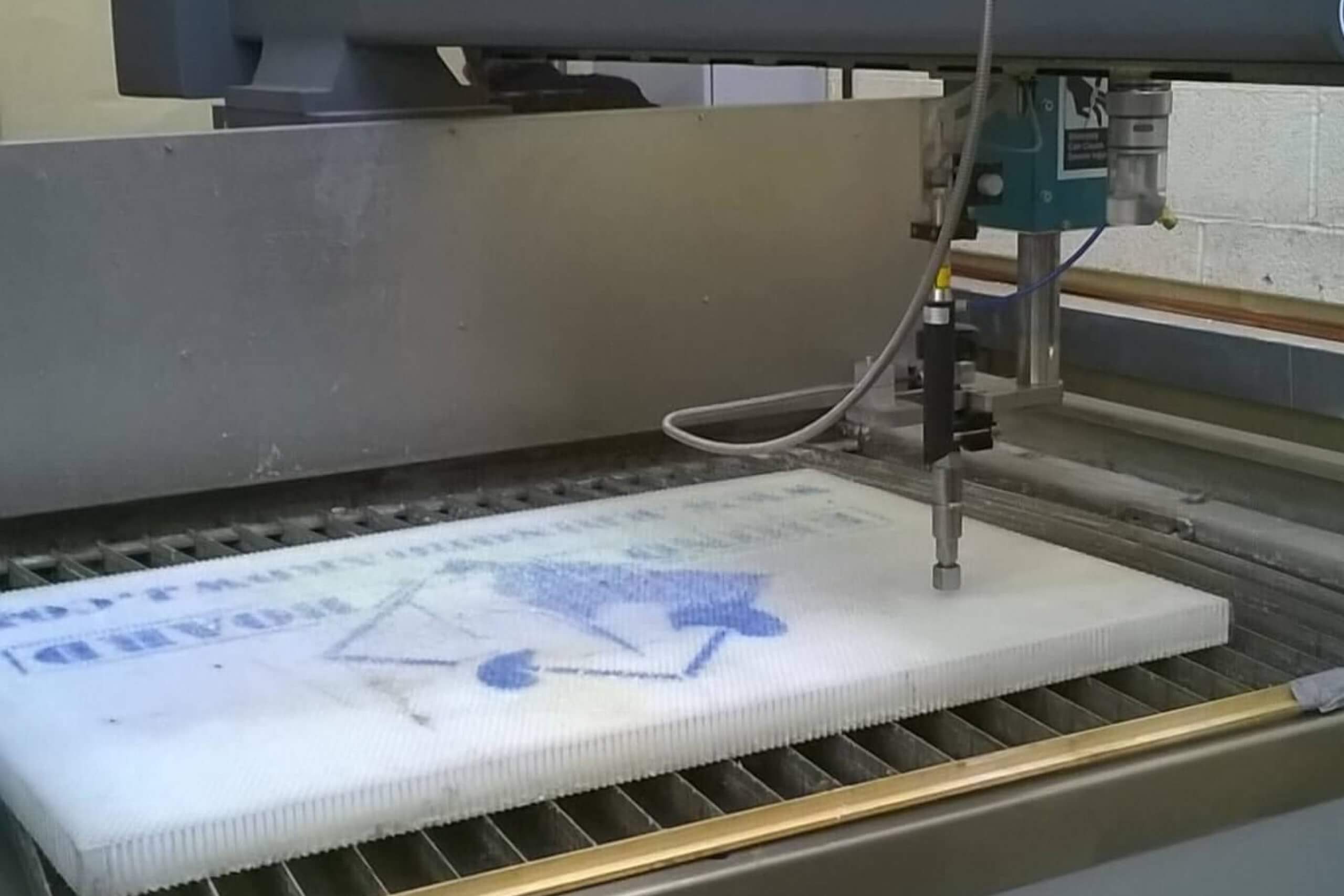 Machine with nozzle cutting white material, industrial setting.