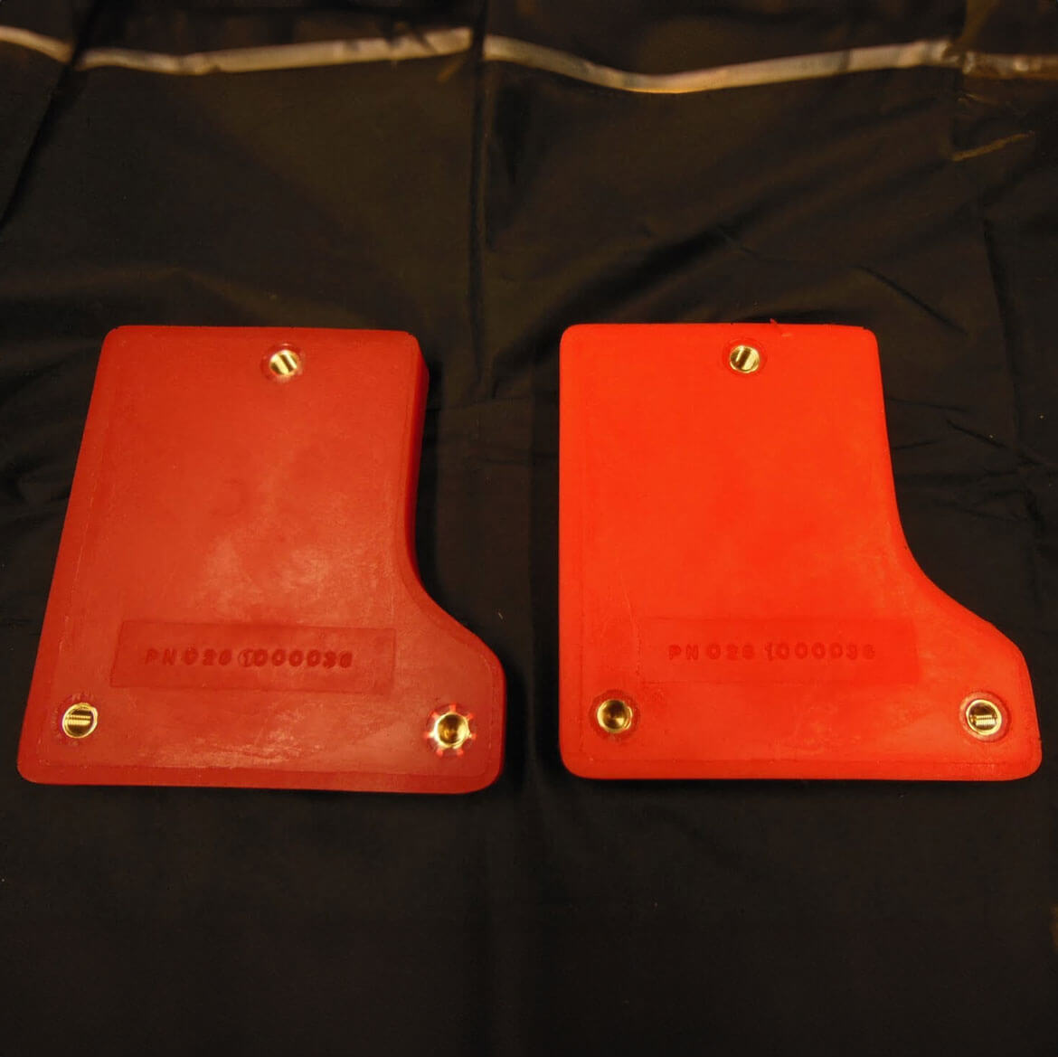 Red plastic mud flaps with bolts, lying on fabric.