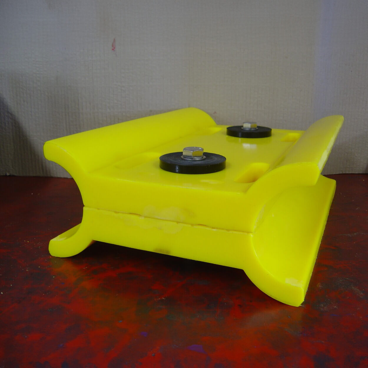 Yellow plastic object with two knobs, resting on red surface.