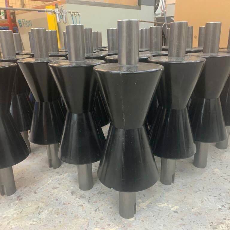 Conical black objects stand, arranged closely, on concrete floor.