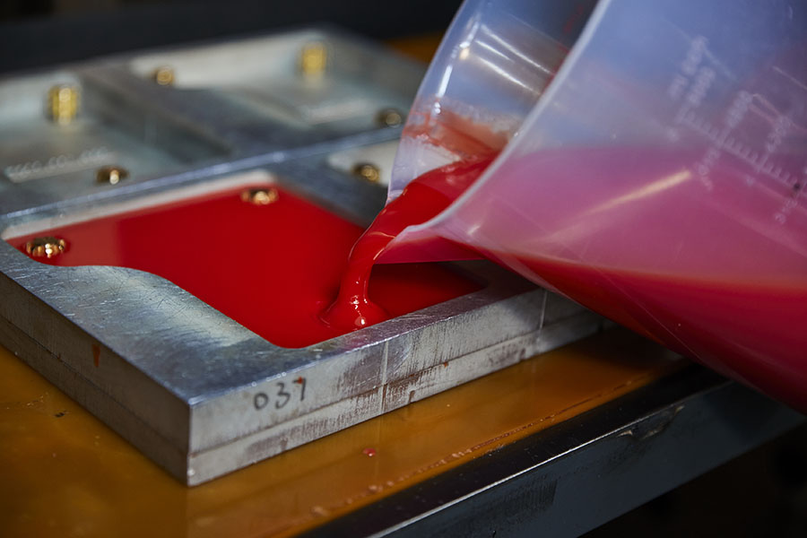 Red liquid pouring into metal mold in workshop setting.