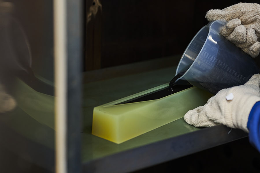Gloved hands pour liquid into a rectangular mold indoors.