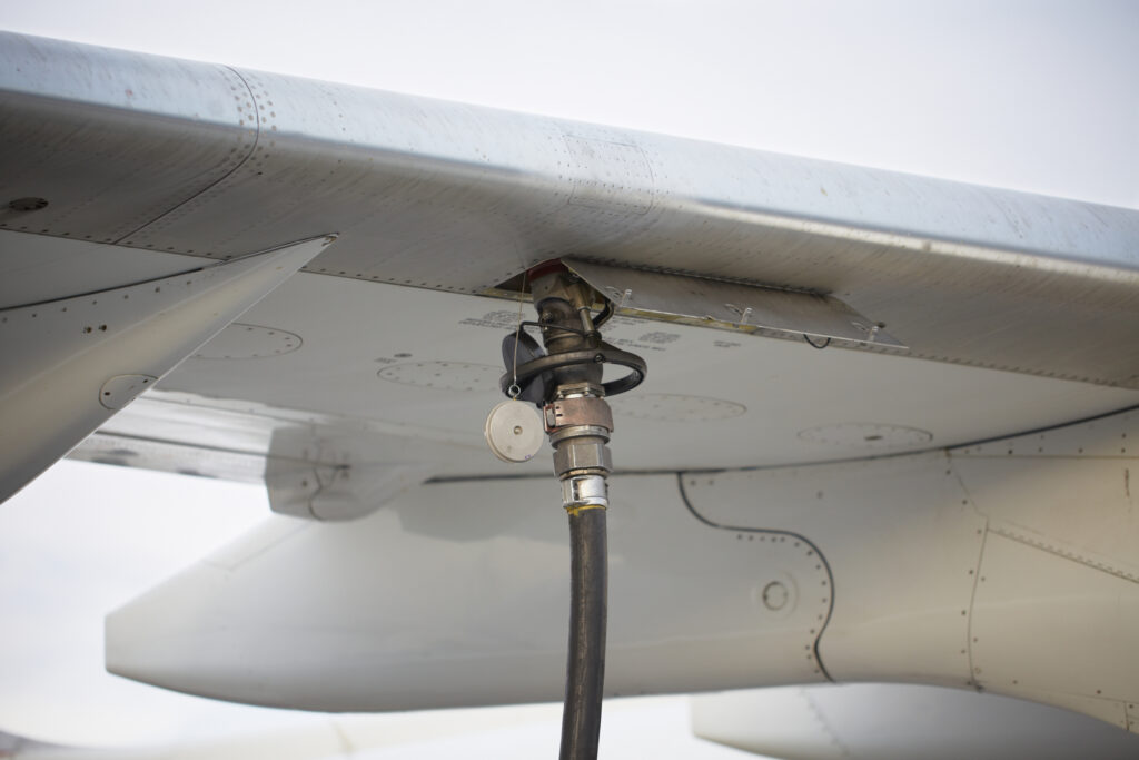 Aircraft wing being refueled with hose in overcast setting.